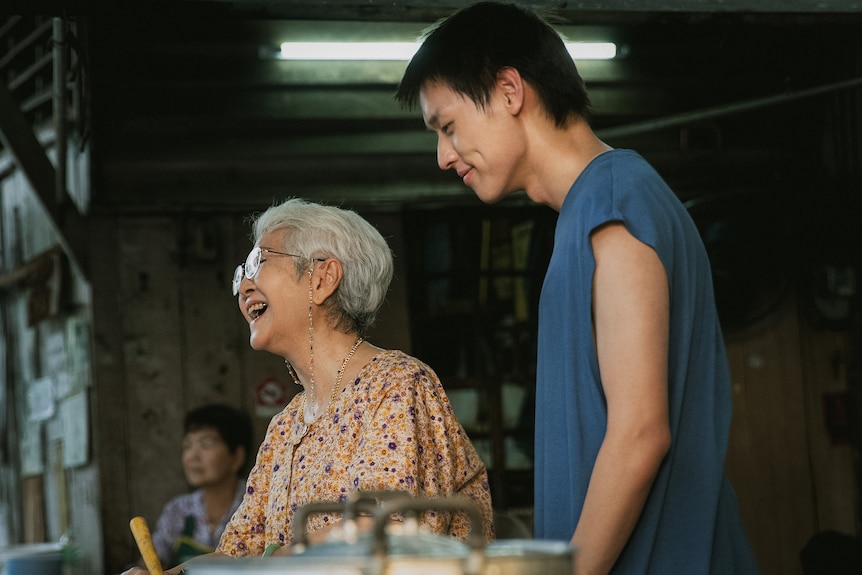 A laughing older woman stands next to a younger man. 