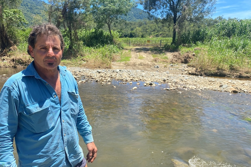 Joe Bugeja standing in front of creek, the gates to his property is visible a short distance behind