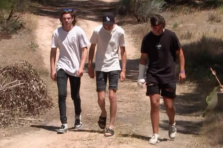 Three men walk along a dirt path through a paddock towards the camera, two with their heads bowed.