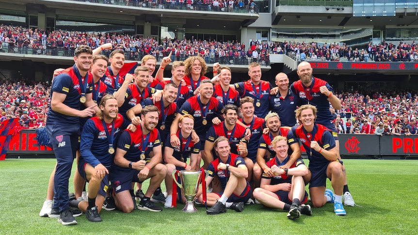 Smiling AFL footballers gather on the ground at the MCG for a group photo with the AFL premiership Cup. 