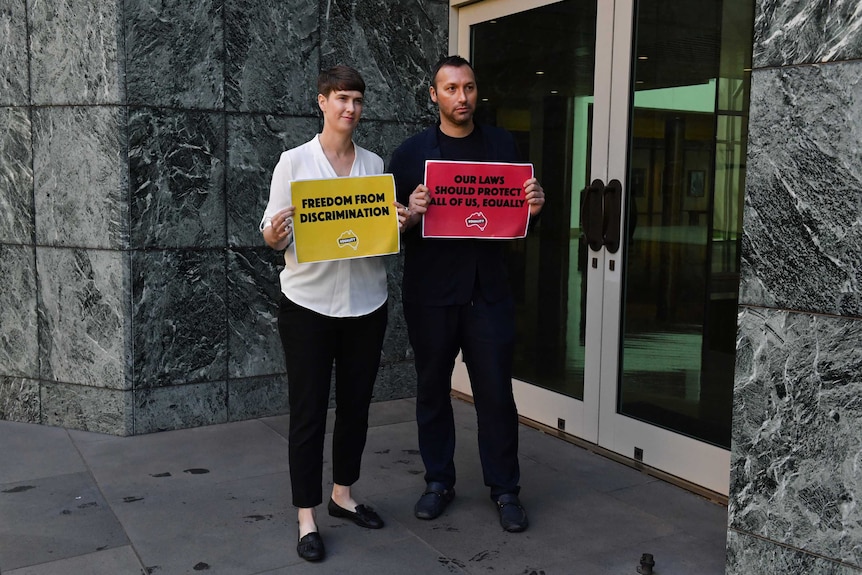 A woman and a man hold signs up