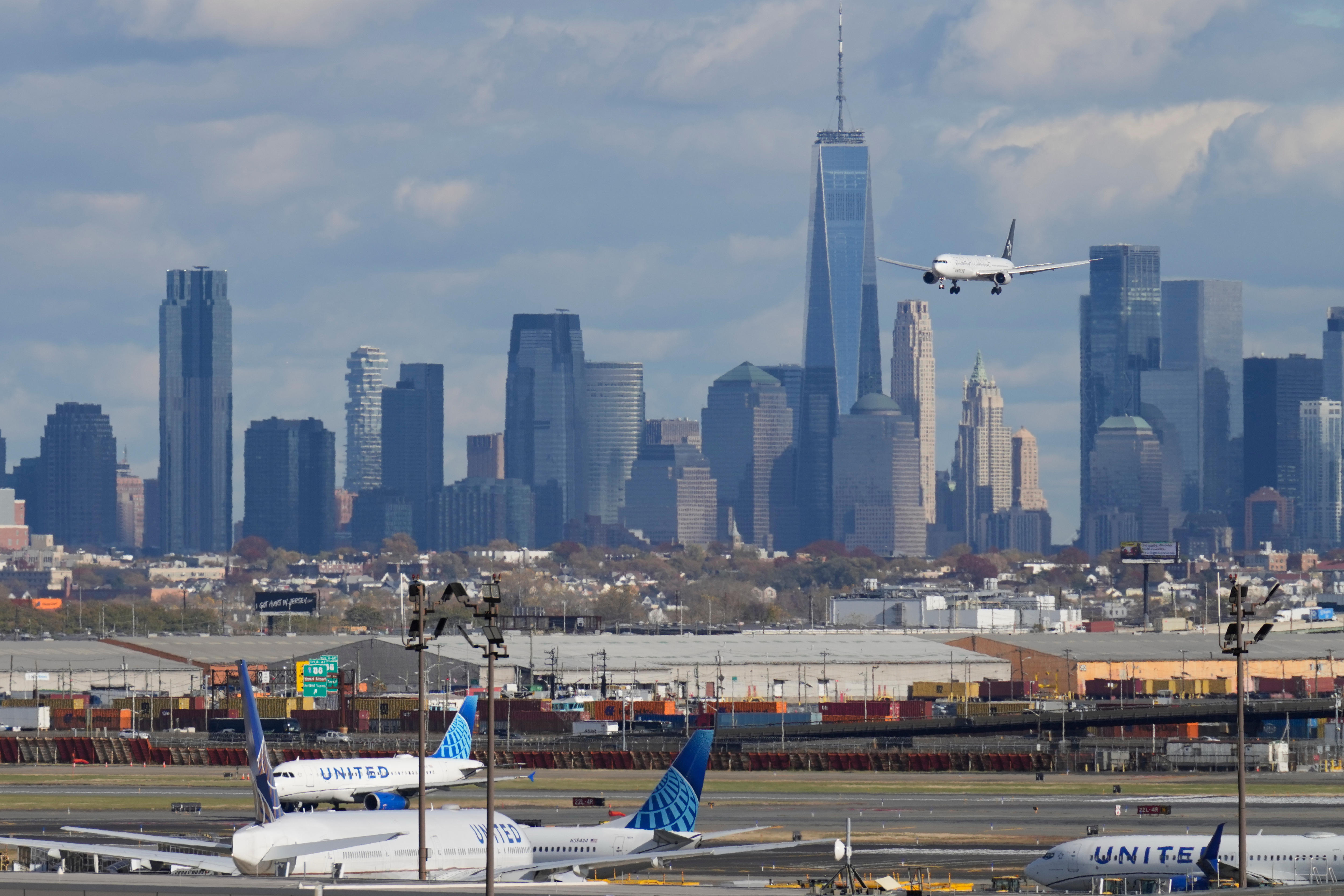 United Airlines planes parked on a tarmac and another flight preparing to land, in front of the New York City skyline