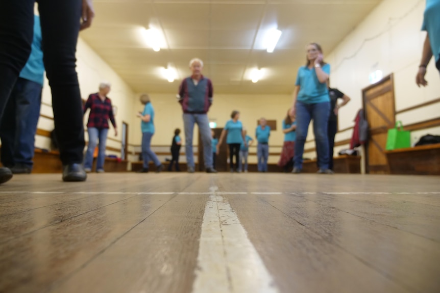 A group of people stand in a hall with a wooden floor.