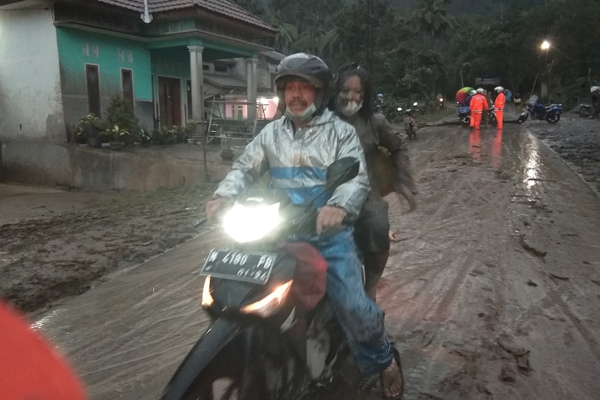 People ride a motorbike on a road that is covered with volcanic ash