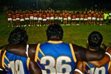 Footballers line up before a game in Kununurra, one team wears red and white, the other blue and yellow with 36 number visible.