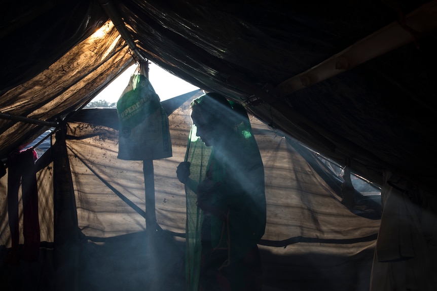 The silhouette of a Rohingya woman in a tent, with smoke in the air