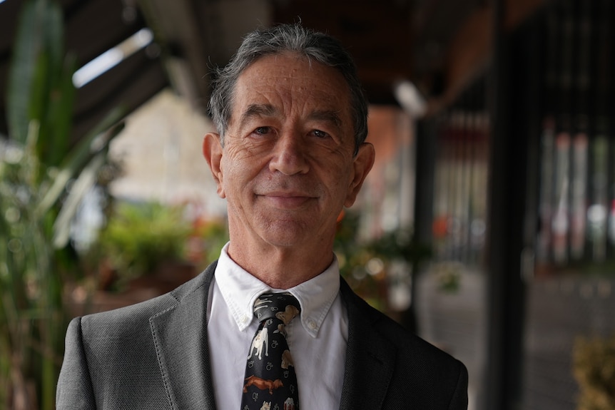 A man in a suit poses for a photo with a serious facial expression.