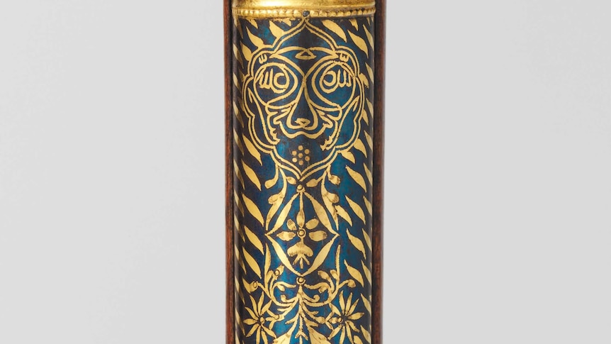 A tiger face and tiger stripes in gold decorate a dark blue section of the barrel of a rifle from the 18th century.
