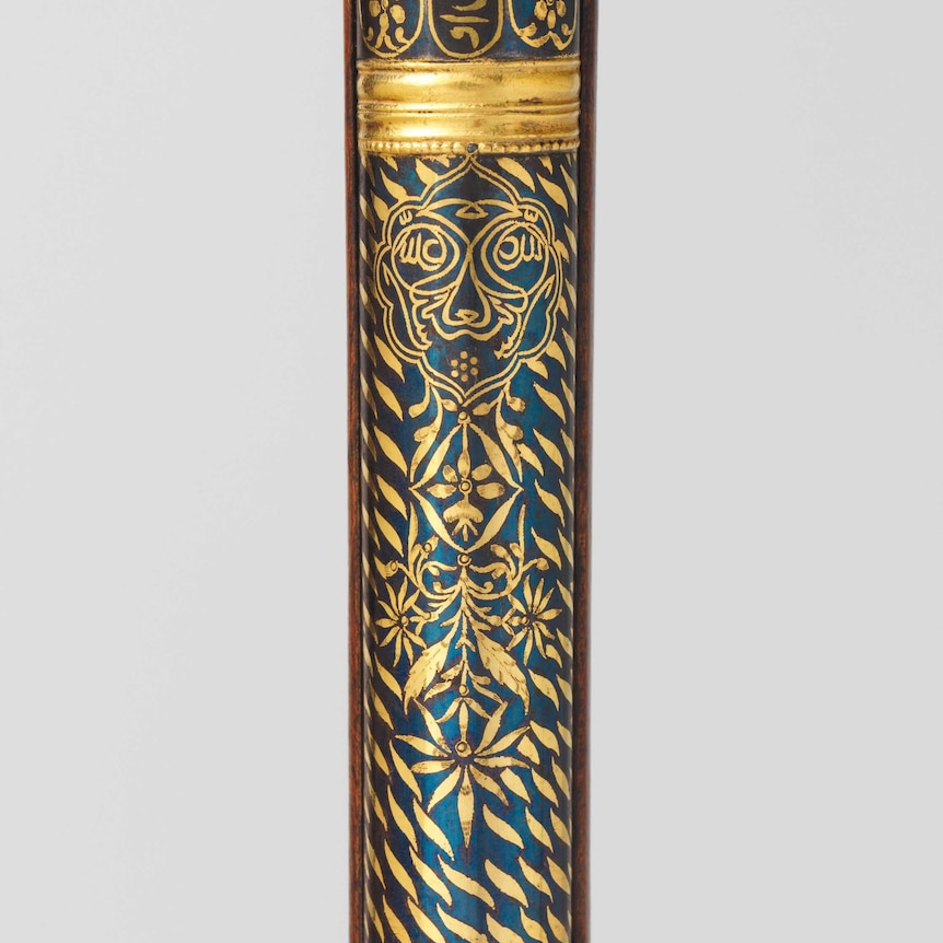 A tiger face and tiger stripes in gold decorate a dark blue section of the barrel of a rifle from the 18th century.