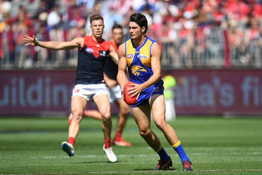 An AFL Eagles player readies to kick a football in front of a Melbourne player.