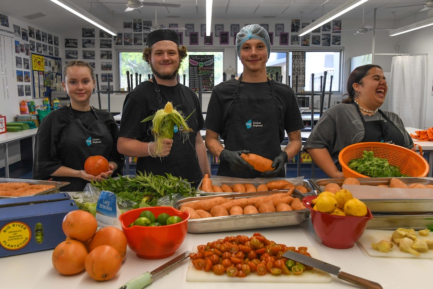 Four young adults holding produce smile at the camera