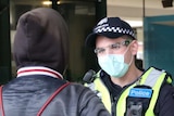 A young man with his back to camera talking to a masked police officer.
