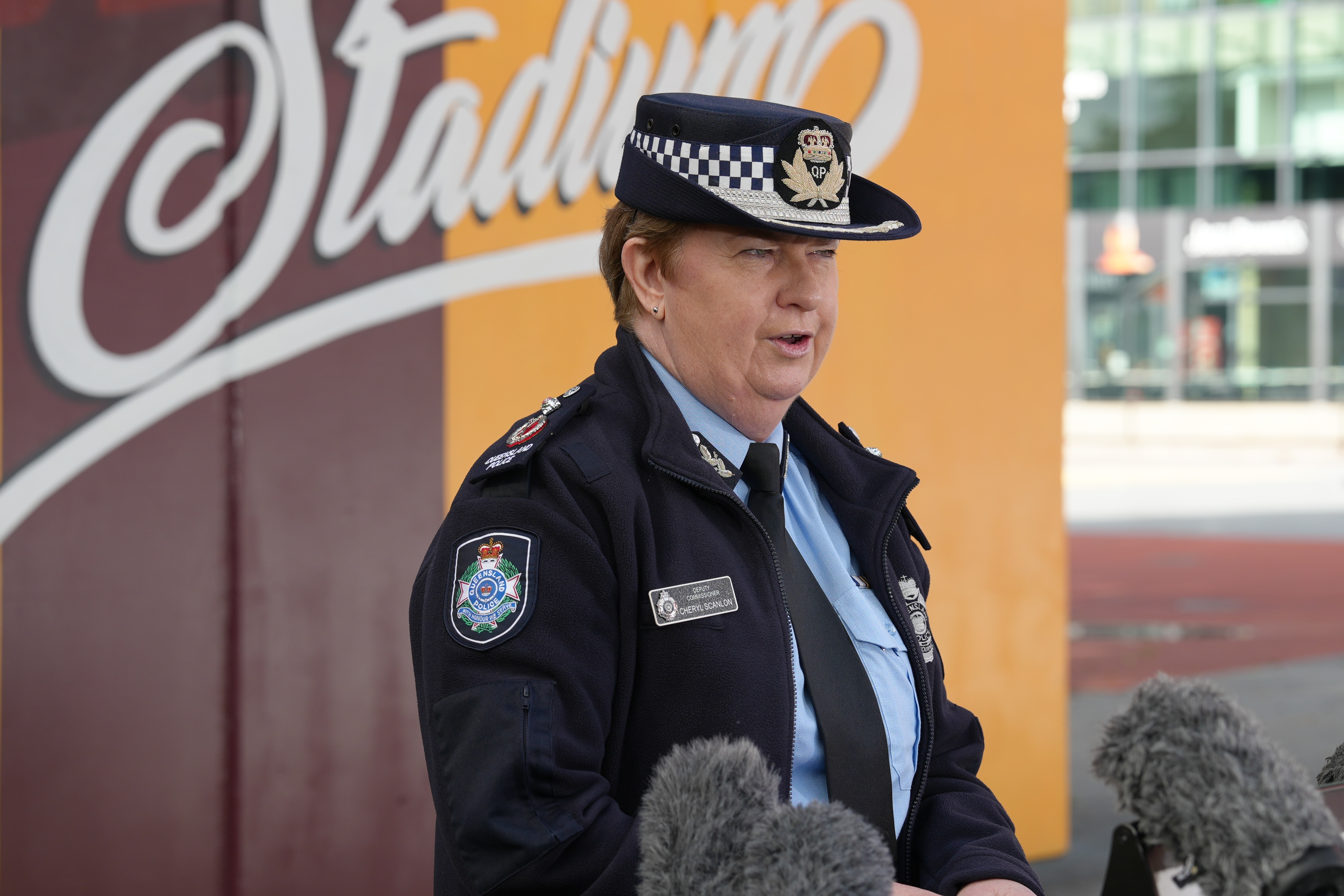 Cheryl Scanlon speaks to media standing in front of a gold and maroon wall outside Lang Park.