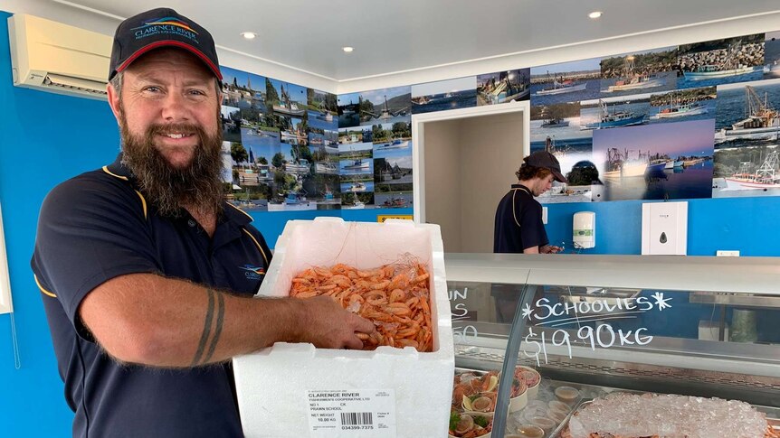 Man smiles at camera while holding a box of prawns.