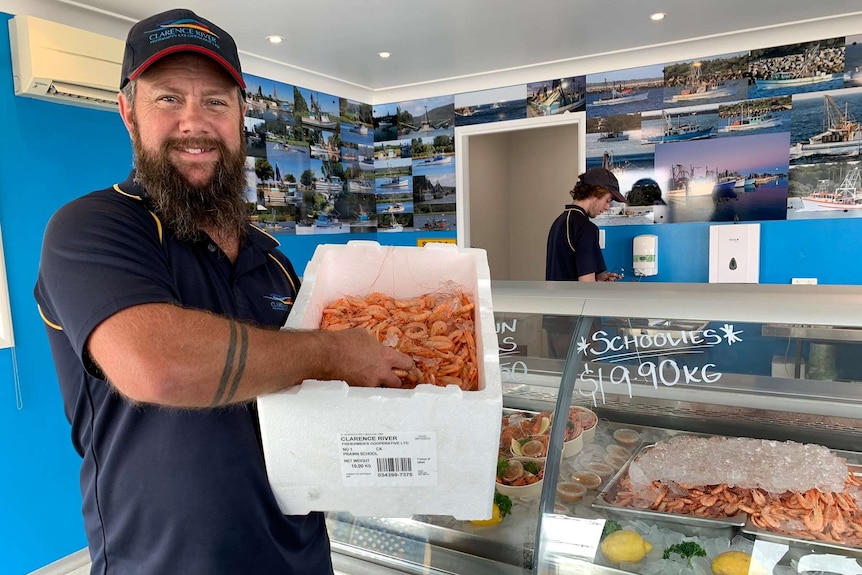 Man smiles at camera while holding a box of prawns.