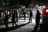 Men stand outside the gates of a hospital in the night.