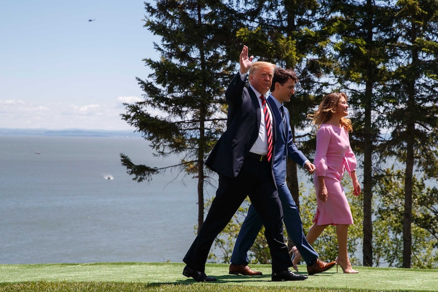 Trump is seen waving as he walks with Justin Trudeau and his wife.