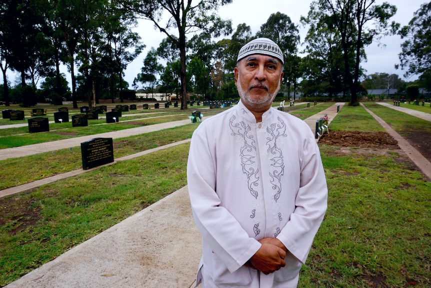 Man wearing white standing in front of cemetery.