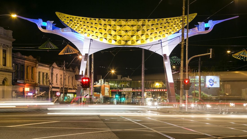 At night, you view a large public sculpture in the shape of an upturned fishing boat hanging over a large intersection. 