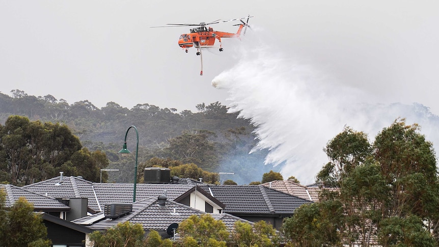 Water falls from an orange chopper into the roofs of suburban homes surrounded by trees.