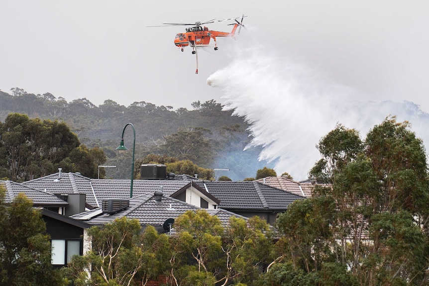 Water falls from an orange chopper into the roofs of suburban homes surrounded by trees.