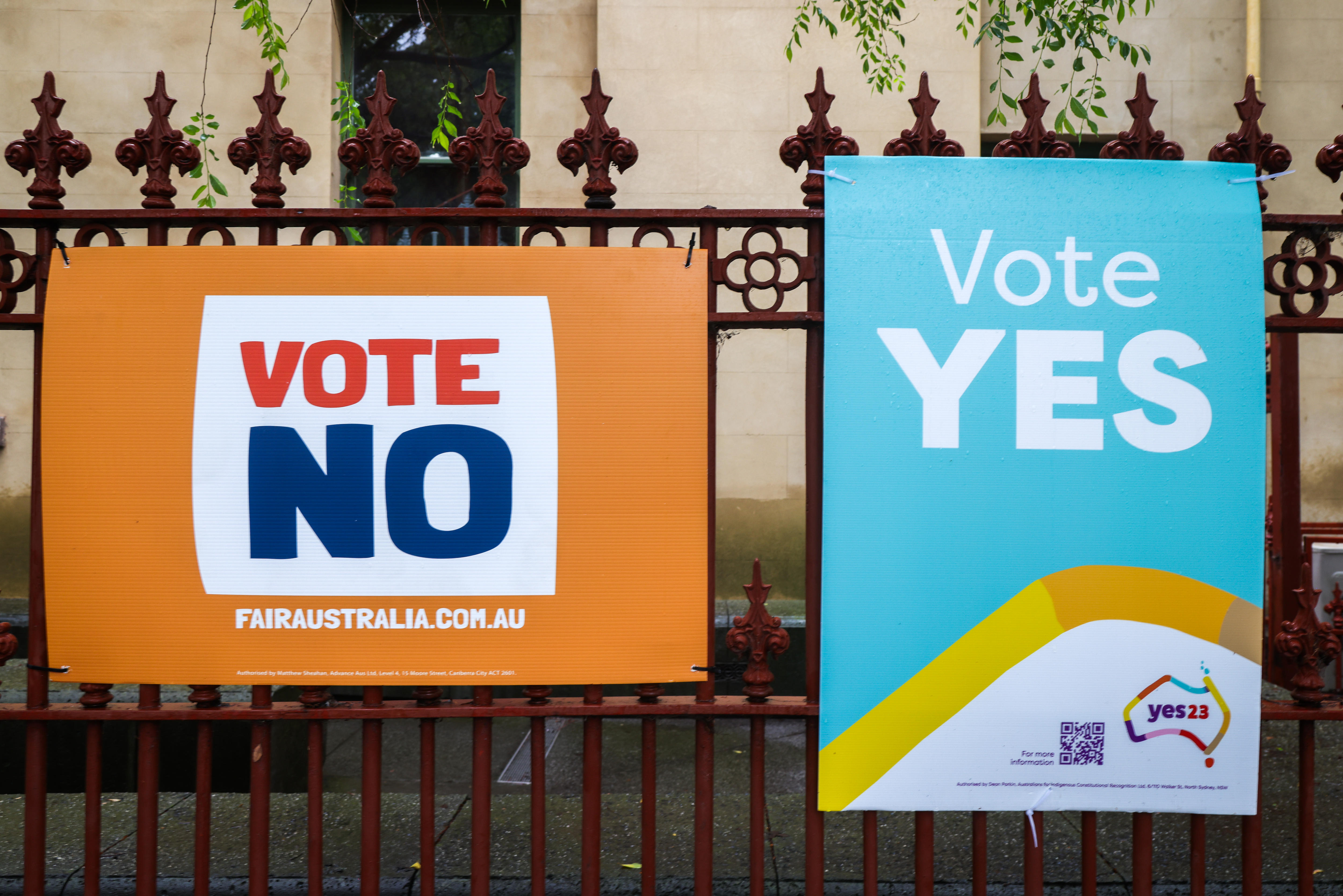 Two separate corflutes on an iron gate read 'VOTE NO' and 'VOTE YES'.
