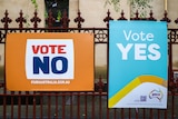 Two separate corflutes on an iron gate read 'VOTE NO' and 'VOTE YES'.