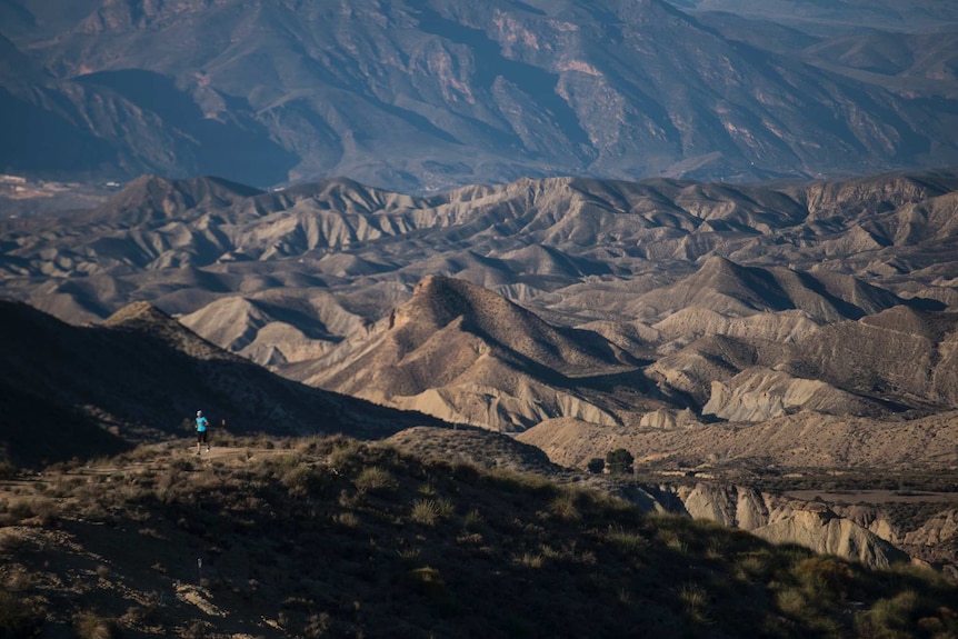 A person cuts a small figure against a backdrop of curved landscape and mountains