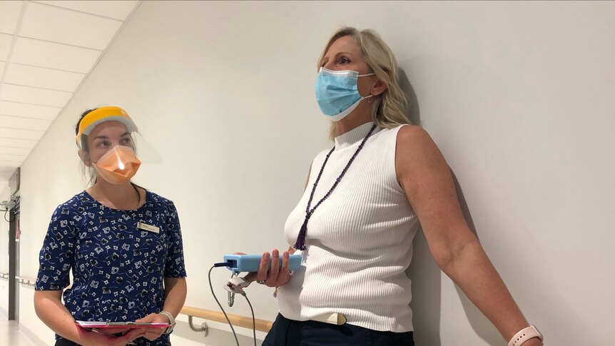 A woman wearing a white top stands next to a healthcare professional in the COVID ward