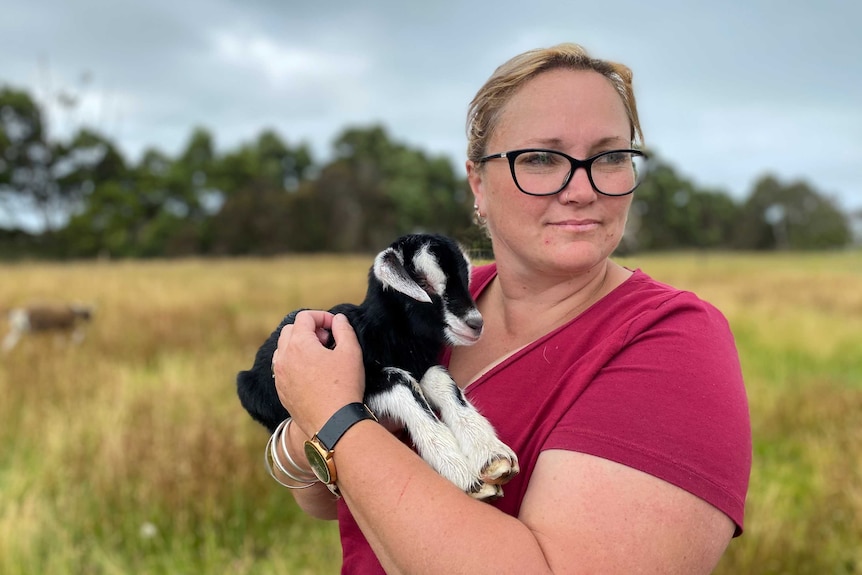 Alyssia Coates holds a young goat at her new farm at Smithton Airport