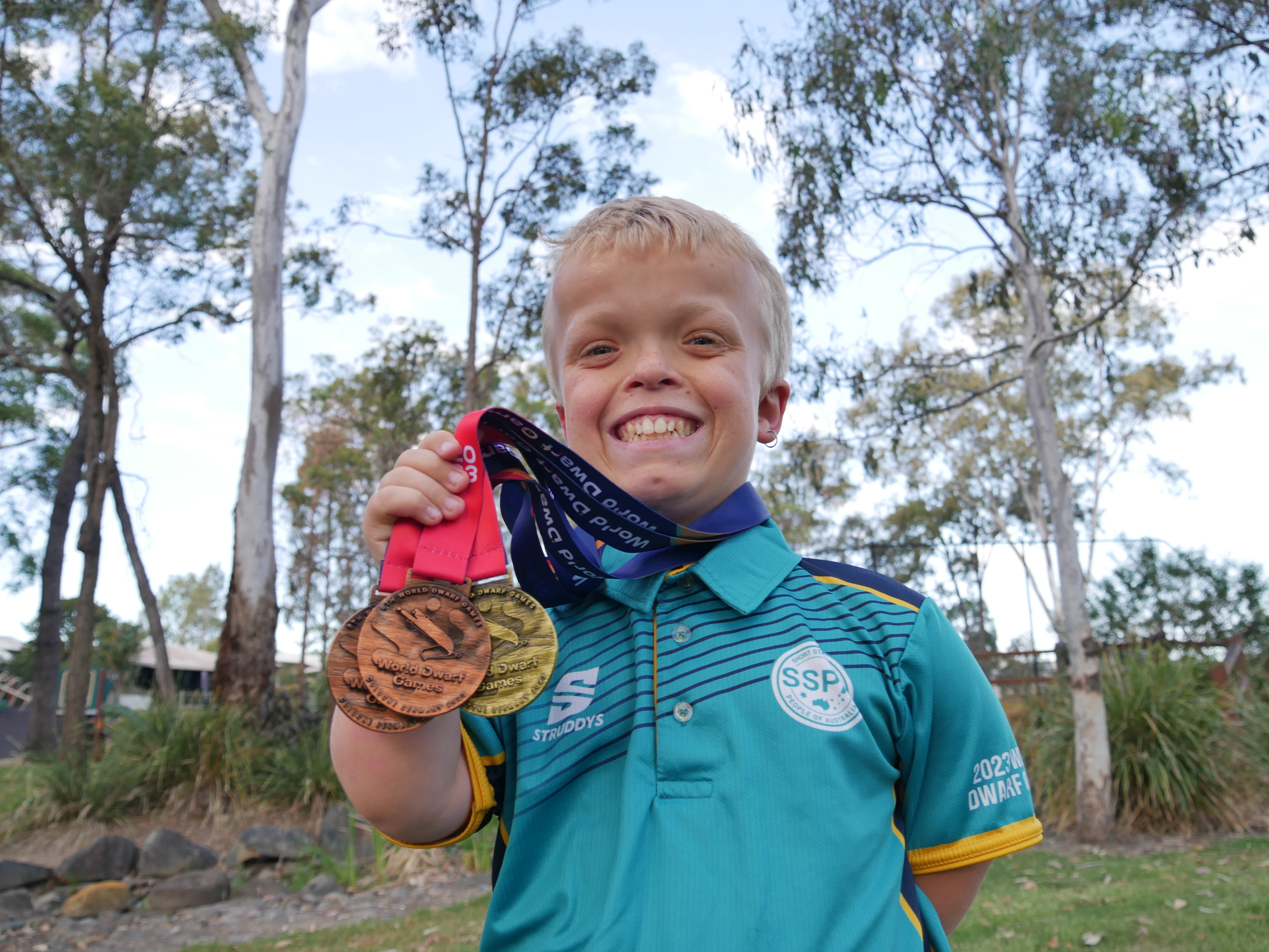 boy holding three medals and smiling