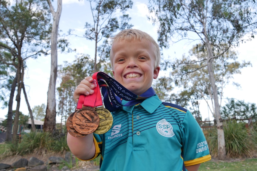 boy holding three medals and smiling