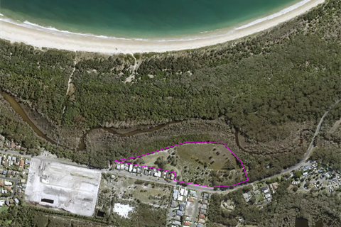 An aerial image showing a section of bushland and some houses, just behind a beach.