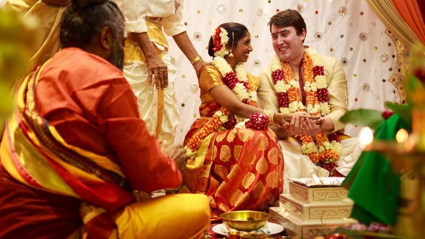 Ahalya Krishinan and Ryan Brown smile at each other during a Hindu wedding.