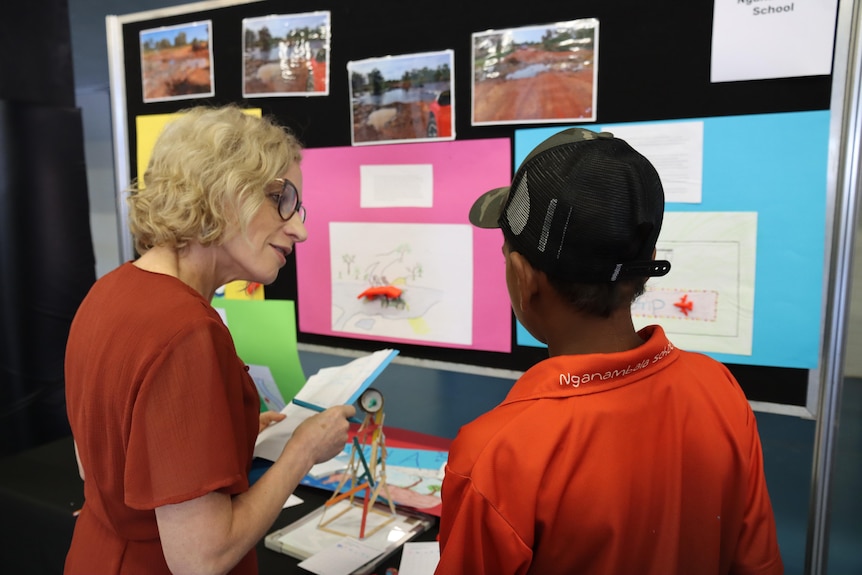 An Aboriginal boy in a school uniform speaks to a woman about a science display