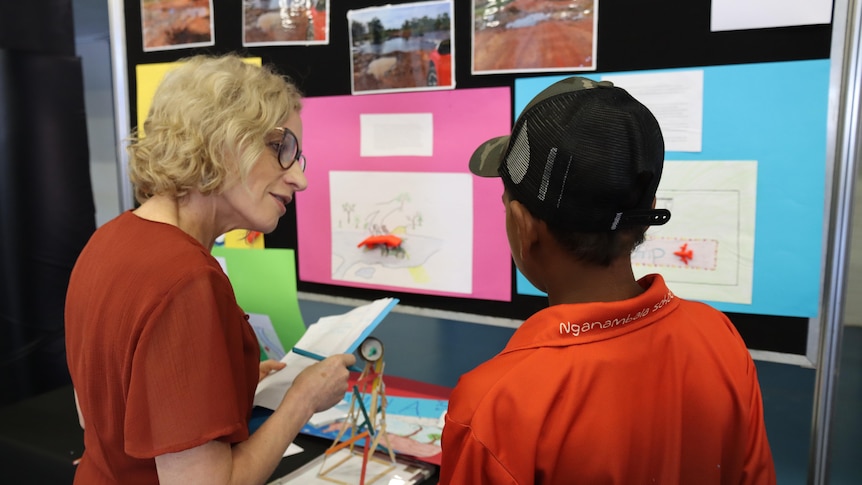 An Aboriginal boy in a school uniform speaks to a woman about a science display
