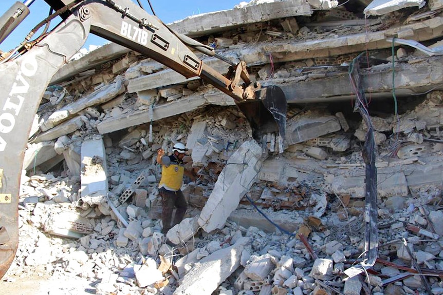 A worker in a helmet and a crane in the rubble of a destroyed building