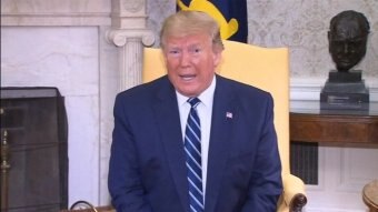 Donald Trump sitting in a yellow chair with a fireplace in the background.