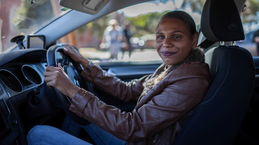 A young Indigenous woman wearing a brown leather jacket sitting in a car.