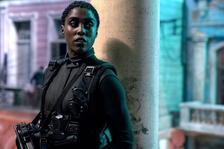 A black woman with short, curly hair in full battle gear looks to her left as she stands next to a concrete pole