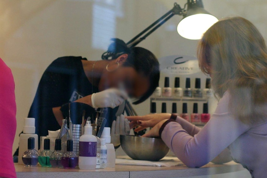 An unidentifiable woman works on another woman's nails at a generic nail salon