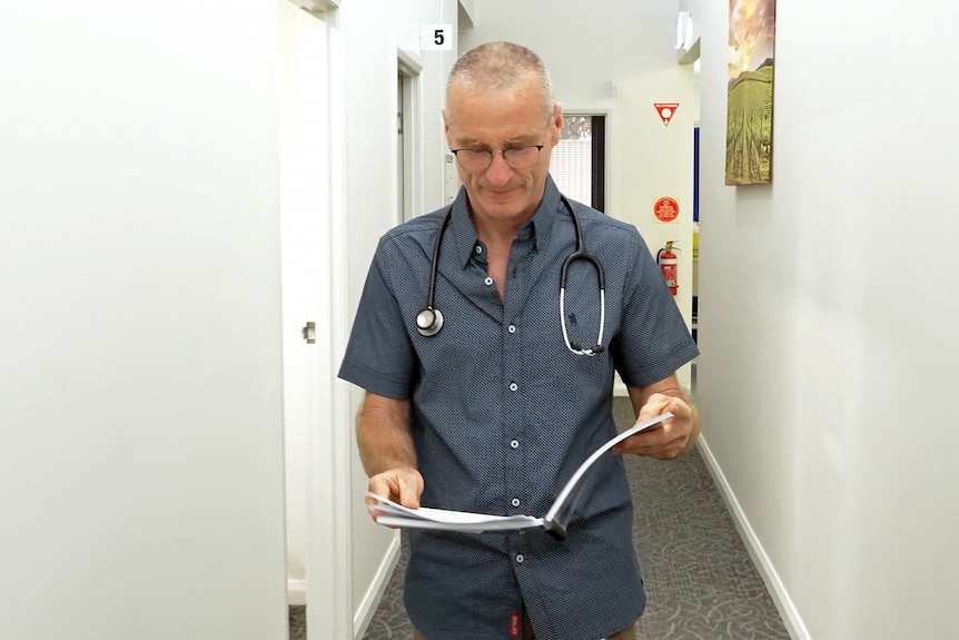 一名男子手上戴着听诊器，沿着走廊走着，读着一个文件夹。