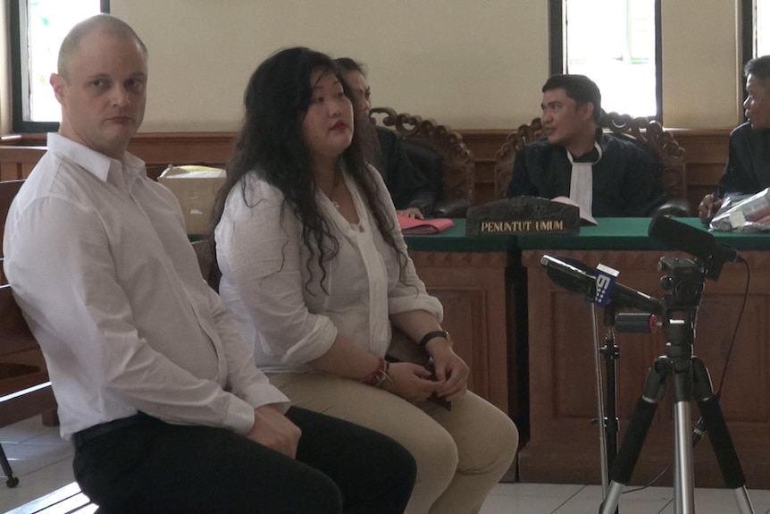 Isaac Emmanuel Roberts sits next to a woman in a courthouse in Denpasar.