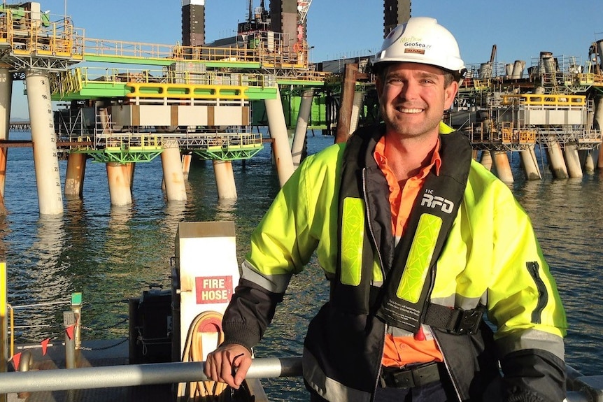 Daniel Bradshaw stands on a dock in workman's gear including high-vis jacket and hard hat.
