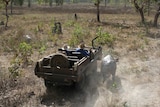 A stripped-down jeep drives alongside a running water buffalo through scrub.