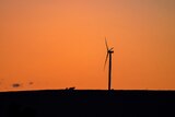 The silhouette of a single wind turbine on a hill at sunset