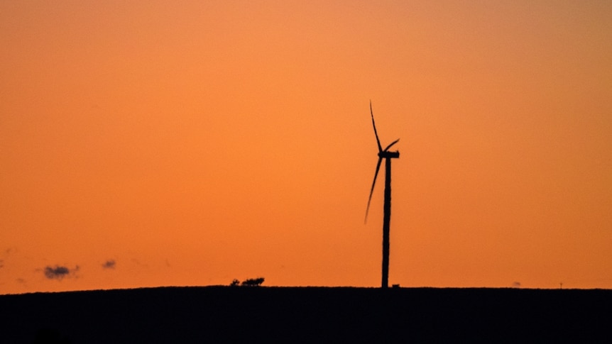 The silhouette of a single wind turbine on a hill at sunset