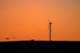 The silhouette of a single wind turbine on a hill at sunset