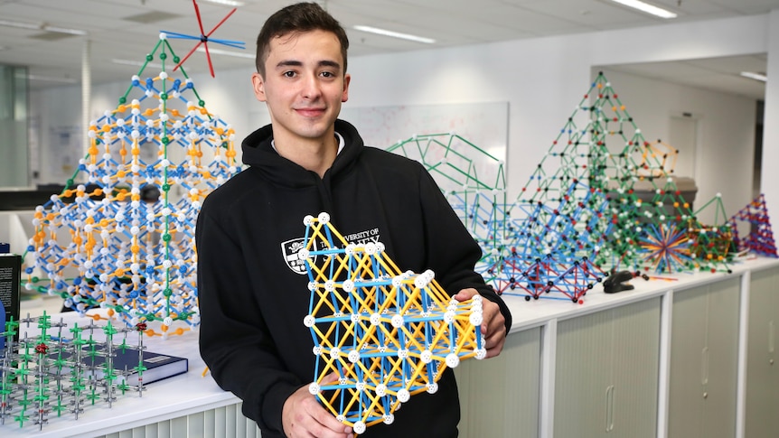 A young man holds a 3D plastic model.