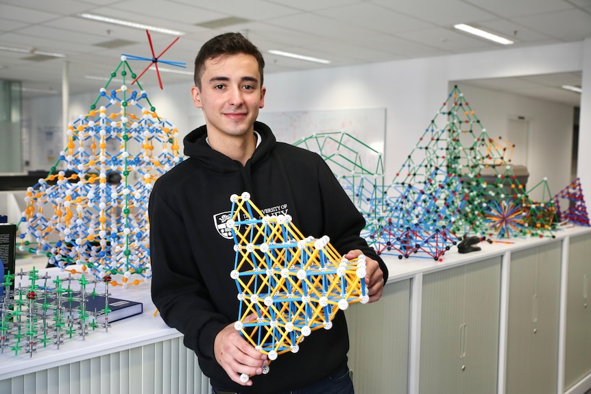 A young man holds a 3D plastic model.